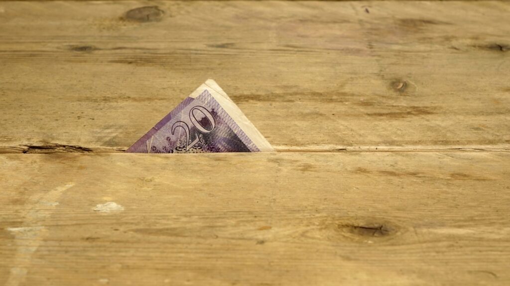 A twenty currency note partially hidden between wooden floorboards