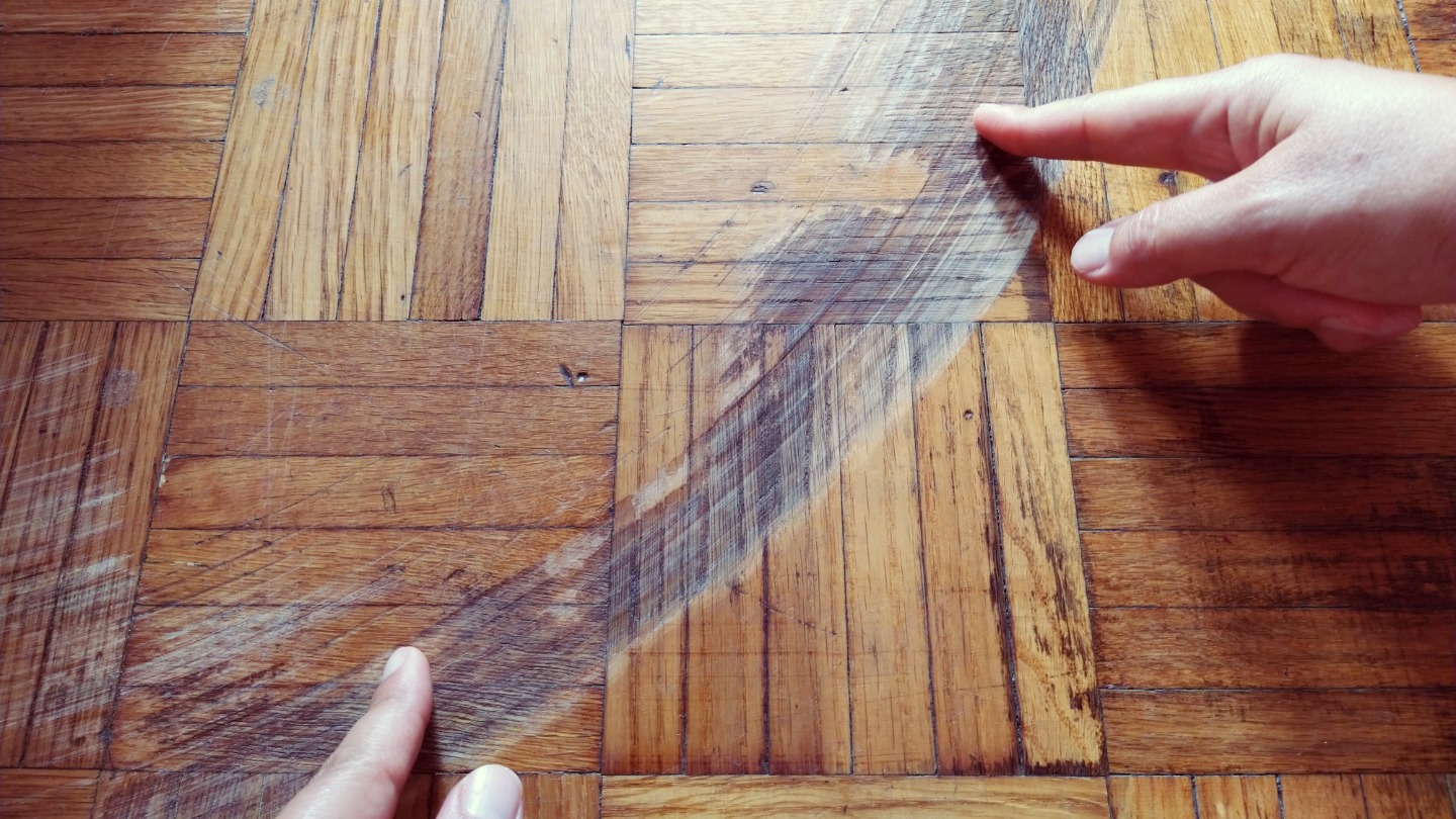 Fingers pointing to a dusty section on a wooden parquet floor