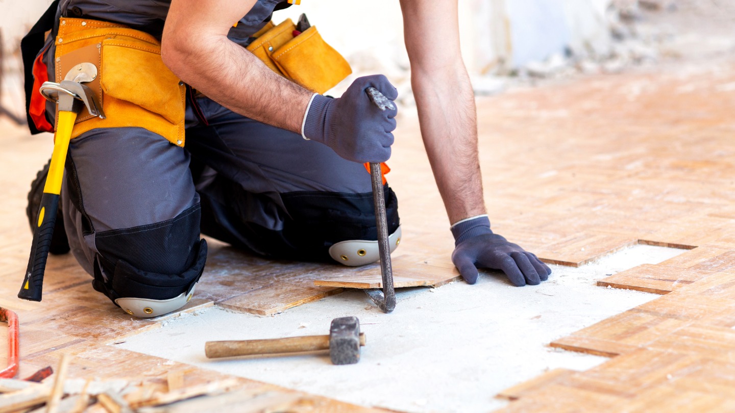 Worker replacing wooden floor tiles with tools