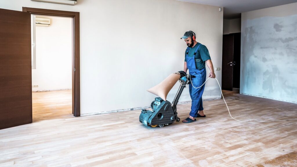 Man using a floor sanding machine in an empty room