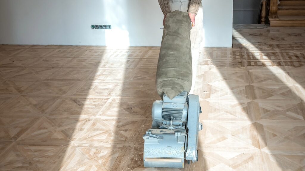 Person using a floor sander on a wooden parquet floor