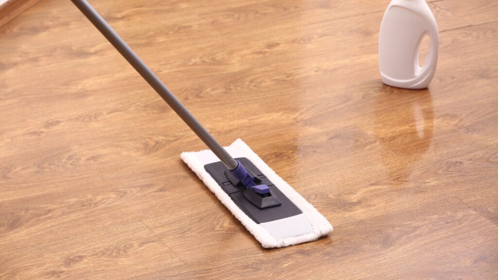 Mop cleaning a wooden floor with a bottle of cleaner