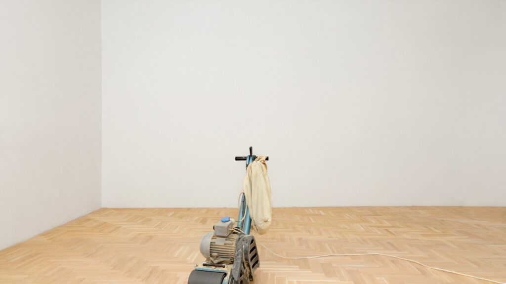 A floor sander placed on a wooden parquet floor in an empty room