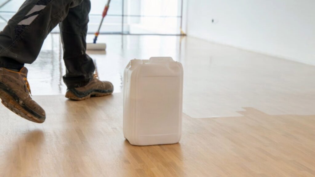 Worker applying varnish on a wooden floor with a roller